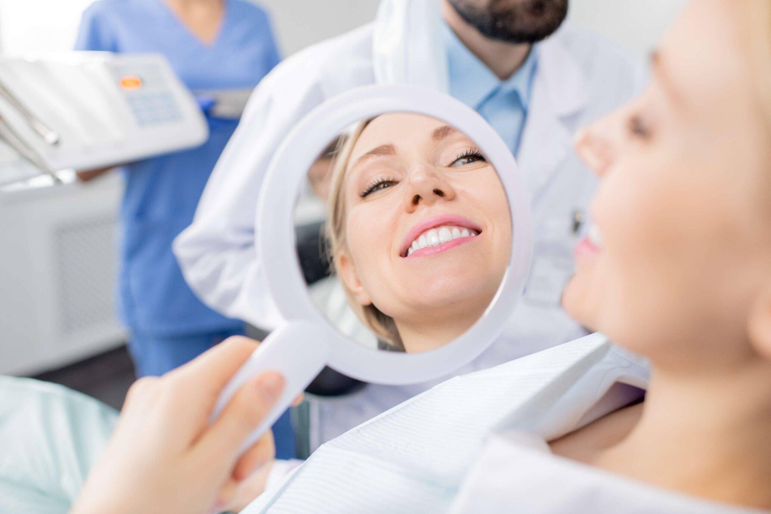 Patient smiling and checking teeth in a dental mirror.